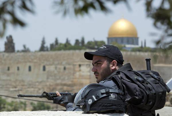 epa04268673 An Israeli riot policeman looks over as Palestinians prayed in the street of the neighborhood of Ras al-Amud, with the Dome of the Rock on the Haram el-Sharif (The Noble Sanctuary) behind, in East Jerusalem, 20 June 2014. Israeli security forces limited attendance to Friday prayers in al-Aqsa Mosque to men over 50 in the belief clashes would start due to increased tensions and clashes since three Israeli teenagers went missing on June 12. Two Palestinians were killed in clashes in the West Bank early today.  EPA/JIM HOLLANDER