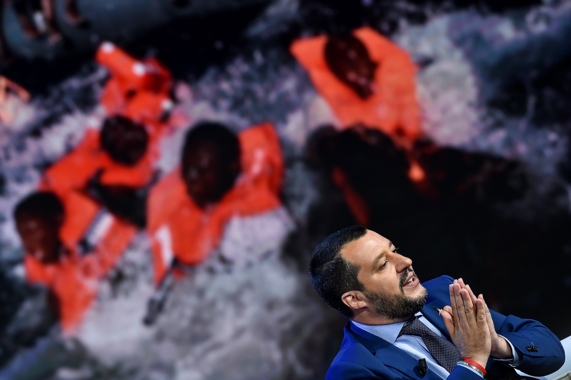 TOPSHOT - Italy's Interior Minister and Deputy Prime Minister Matteo Salvini speaks during the Italian talk show "Porta a Porta", broadcast on Italian channel Rai 1, in Rome, on June 20, 2018, as picture of migrants is seen in the background. (Photo by Andreas SOLARO / AFP)        (Photo credit should read ANDREAS SOLARO/AFP/Getty Images)